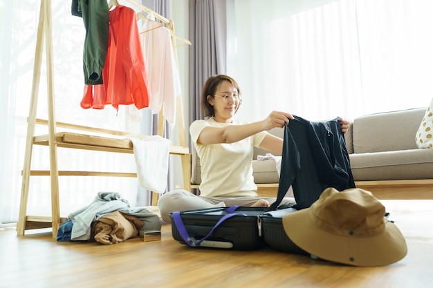 Heureuse jeune femme mains emballer des vêtements dans des bagages de voyage sur le lit à la maison