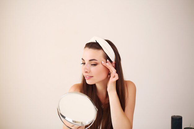 Heureuse jeune femme mettant la crème pour le visage pour faire des soins de la peau saine matin