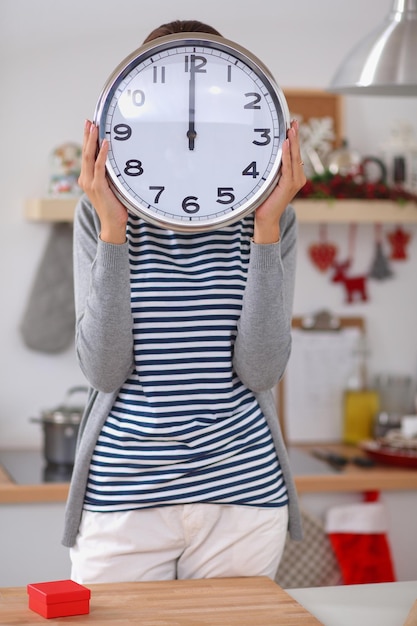 Photo heureuse jeune femme montrant l'horloge dans la cuisine décorée de noël