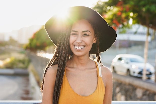 Heureuse jeune femme multiraciale souriante à la caméra dans la ville avec coucher de soleil en arrière-plan