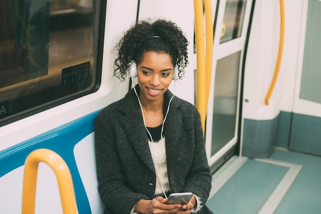 Heureuse jeune femme noire assise dans le métro en écoutant de la musique