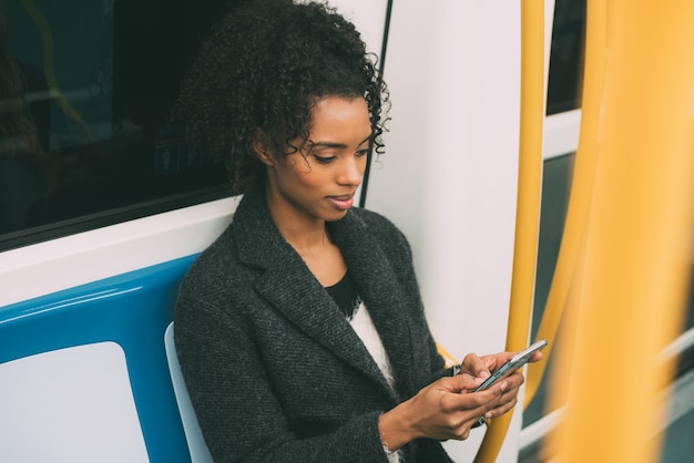 Heureuse jeune femme noire assise dans le métro sur le téléphone mobile