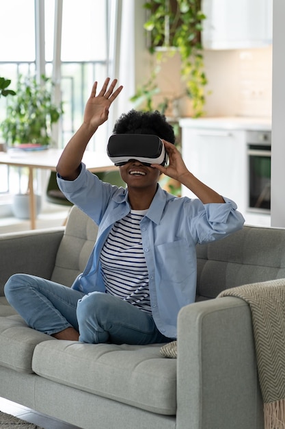 Heureuse jeune femme noire excitée profitant d'une expérience de magasinage en réalité virtuelle tout en se reposant à la maison