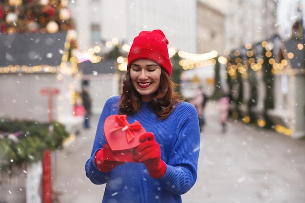 Heureuse jeune femme ouvrant une boîte-cadeau avec un ruban à la foire de Noël. Espace libre