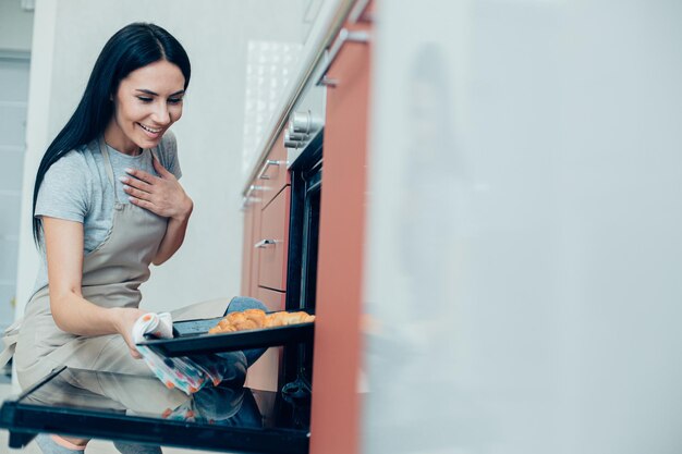 Heureuse jeune femme ouvrant le four et regardant le plat de cuisson avec de la pâtisserie avec un sourire. Bannière de site Web