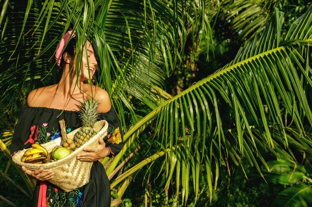 Heureuse jeune femme avec un panier plein de fruits exotiques