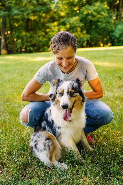 Heureuse jeune femme passant du temps avec un joli chien de berger australien tacheté dans un pré vert sur