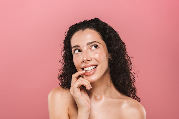 Heureuse jeune femme avec une peau saine posant isolée sur un mur rose.