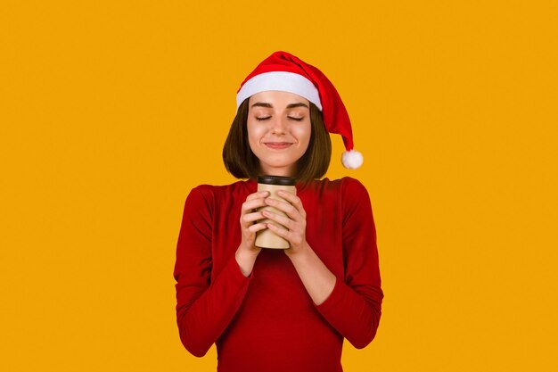 Heureuse jeune femme portant un chapeau de Père Noël buvant une odeur de cacao savoureux