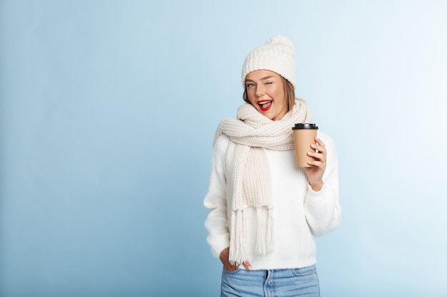 Heureuse jeune femme portant un pull et un chapeau, tenant un café à emporter