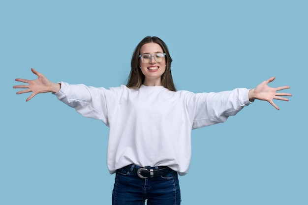 Heureuse jeune femme posant avec les bras tendus vous embrassant souriant à la caméra sur fond bleu