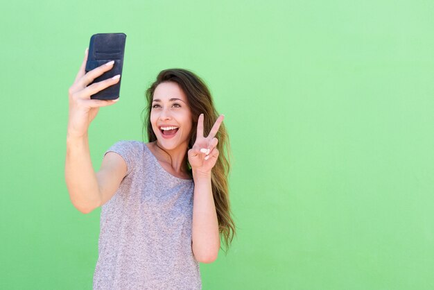 Heureuse jeune femme prenant selfie avec signe de paix main