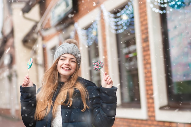 Heureuse jeune femme profitant des vacances d'hiver avec une sucette colorée dans la rue. Espace libre