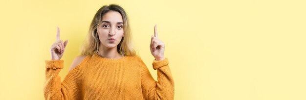 Heureuse jeune femme de race blanche dans un pull jaune pointant les doigts vers l'extérieur.