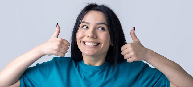 Heureuse jeune femme de race blanche dans un t-shirt bleu faisant signe de pouce vers le haut et souriant Bon travail