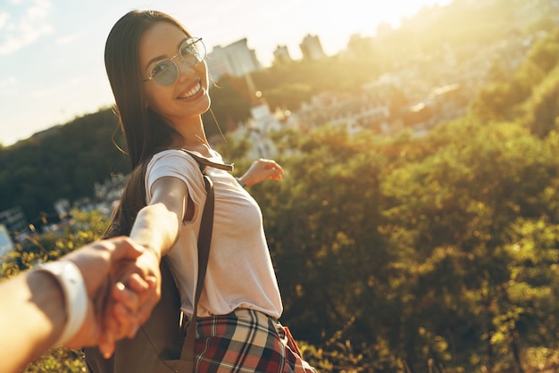 Heureuse jeune femme regardant la caméra et souriant tout en tenant la main de son petit ami