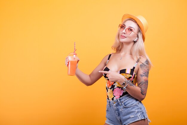 Heureuse Jeune Femme Regardant Le Jus D'orange Frais D'été Pensant Qu'elle Est Sexy En Studio Sur Fond Jaune