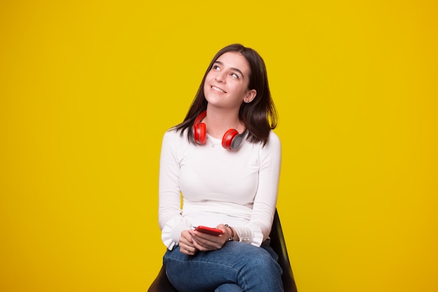 Heureuse jeune femme regardant loin et tenant le smartphone sur fond jaune