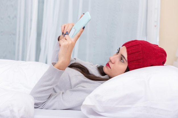 Heureuse jeune femme regardant un téléphone portable au lit