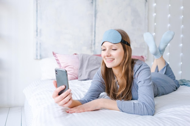 Heureuse jeune femme se détendre en utilisant et en parlant avec un smartphone sur le lit à la maison