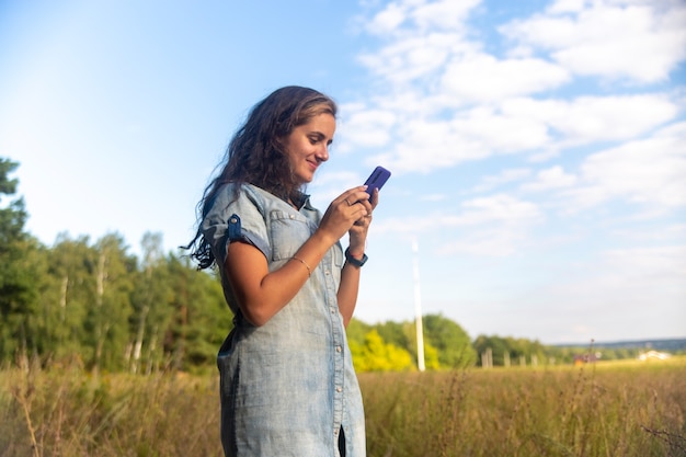 heureuse jeune femme se penche sur le smartphone sur fond de nature aux beaux jours