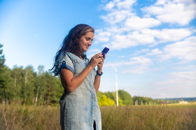 Heureuse jeune femme se penche sur le smartphone sur fond de nature par une journée ensoleillée