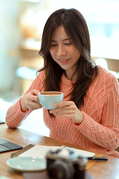 Heureuse jeune femme se relaxant en sirotant un café pour l'après-midi après une dure journée de travail