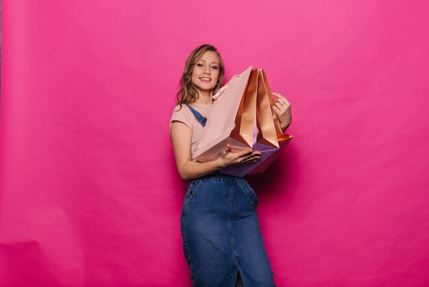 Heureuse jeune femme serrant ses sacs à provisions en souriant et en regardant la caméra