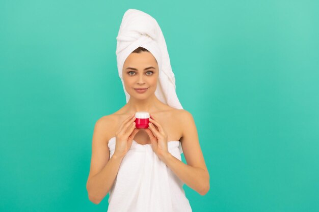 Heureuse jeune femme en serviette avec de la crème pour la peau sur fond bleu