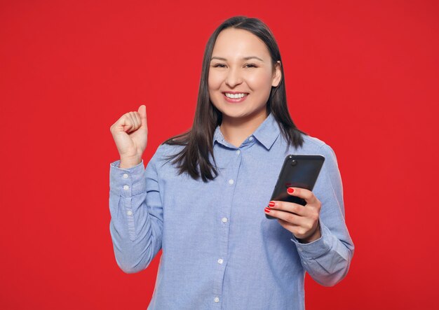 Heureuse jeune femme avec un smartphone à la main sur fond rouge