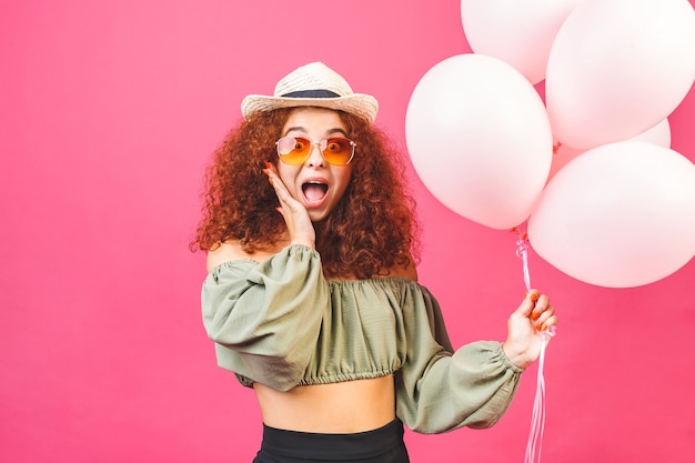 Heureuse jeune femme souriante bouclée avec des ballons isolés sur fond rose