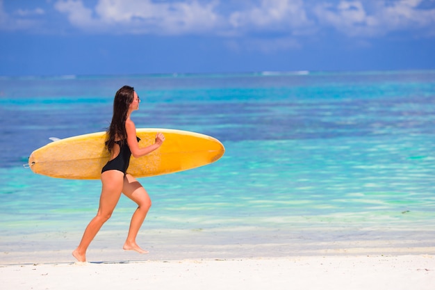 Heureuse jeune femme surf sur la plage avec une planche de surf