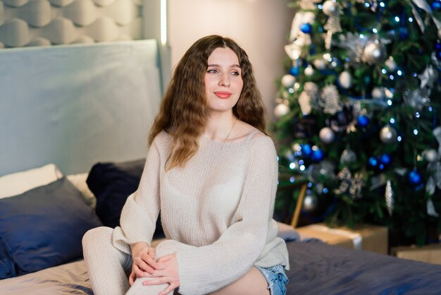 Heureuse jeune femme surprise émotionnelle par l'arbre de Noël dans un salon confortable, concept de bonheur