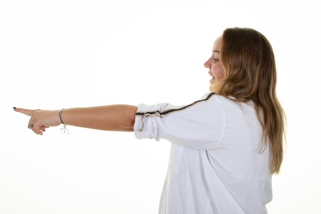 Heureuse jeune femme surprise pointant le profil du doigt droit sur fond blanc