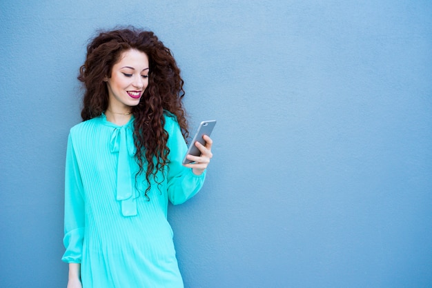 Heureuse jeune femme sur le téléphone mobile sur un mur bleu