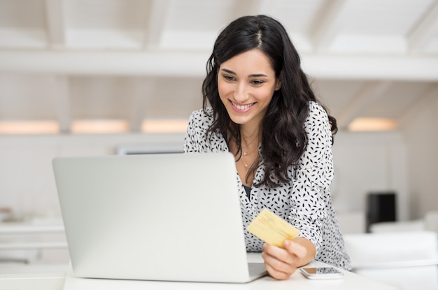 Photo heureuse jeune femme tenant une carte de crédit et achats en ligne à la maison