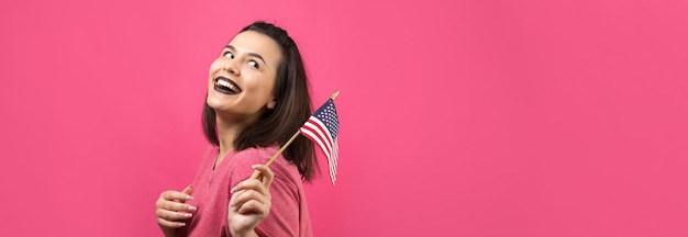 Heureuse jeune femme tenant un drapeau américain sur un fond rose studio