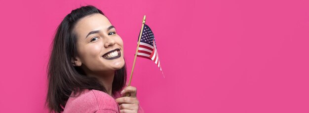 Heureuse jeune femme tenant un drapeau américain sur un fond rose studio