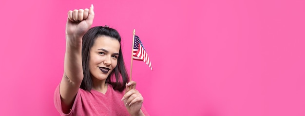 Heureuse jeune femme tenant un drapeau américain sur un fond rose studio