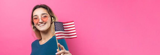 Heureuse jeune femme tenant un drapeau américain sur un fond rose studio