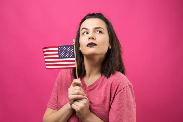 Heureuse jeune femme tenant un drapeau américain sur un fond rose studio