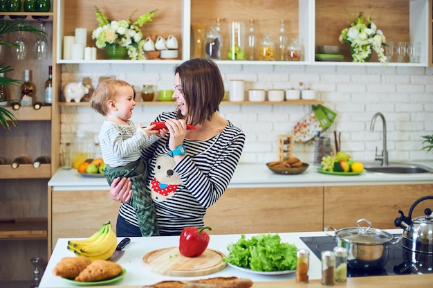 Heureuse jeune femme tenant un enfant de 1 an et cuisiner ensemble dans la cuisine