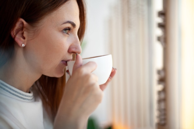 Heureuse jeune femme tenant avec les mains une tasse de café au lait chaud sain