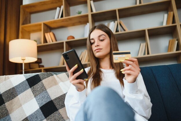 Heureuse Jeune Femme Tenant Un Téléphone Et Une Carte De Crédit Assis Sur Le Canapé Achats En Ligne