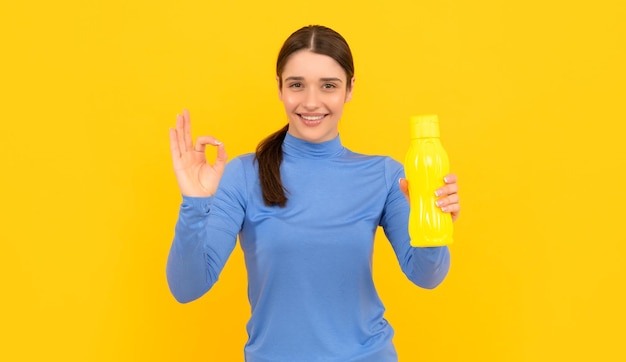 Heureuse jeune femme tient une bouteille de sport avec de l'eau avec une hydratation gestuelle ok