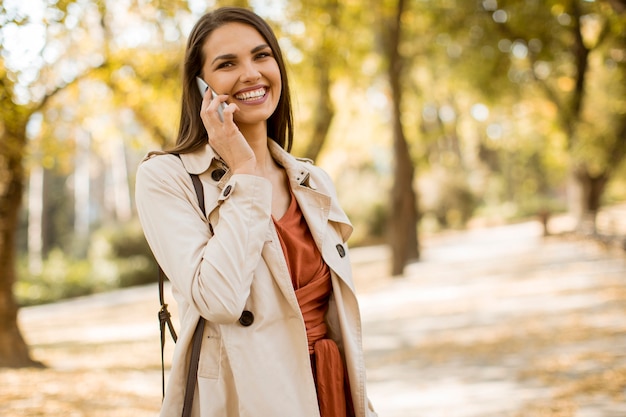 Heureuse jeune femme utilisant un téléphone portable dans un parc en automne par une belle journée