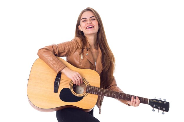 Heureuse jeune femme en veste marron et pantalon noir tenant une guitare sur fond blanc en studio