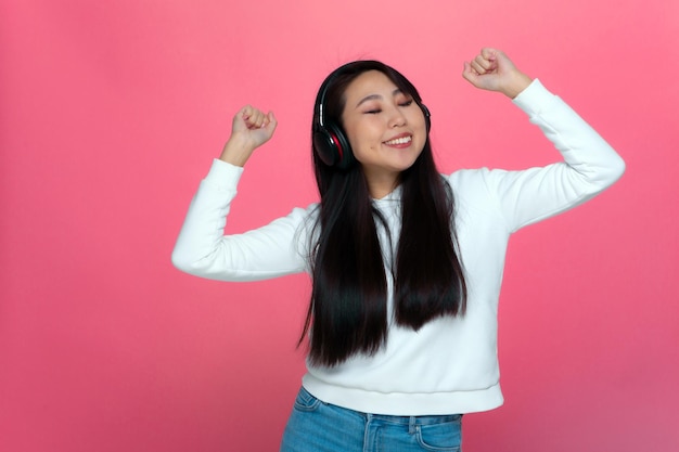 Heureuse jeune fille asiatique dans les écouteurs s'amusant écouter de la musique danse avec les yeux fermés les mains levées