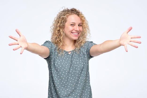 Heureuse jeune fille bouclée avec les mains tendues pour vous embrasser