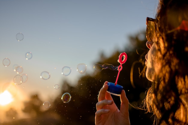 Heureuse jeune fille avec des bulles de savon en automne au coucher du soleil.